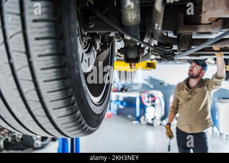 Nahaufnahme der Aufhängung und des Rades eines Fahrzeugs, das auf einer Hebebühne angehoben wurde, in der professionellen Automobilwerkstatt. Kaukasischer Mechaniker bereitet sich auf eine Service-CHEC vor Stockfoto