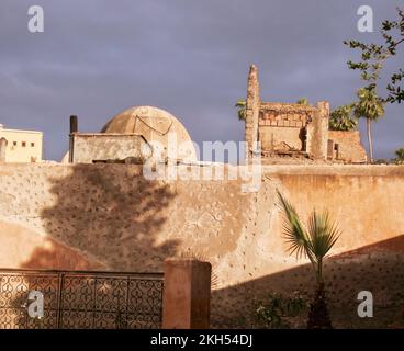 Steinmauer der Medina, mit Kuppel dahinter und dunklem, körnigen Himmel und Schatten von Bäumen, Marrakesch, Marokko Stockfoto