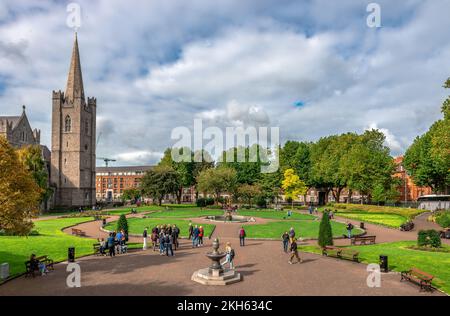 Die Leute genießen einen sonnigen Tag im St. Patrick's Park. Die St. Patrick's Cathedral befindet sich auf der linken Seite. Dublin, Irland. Stockfoto