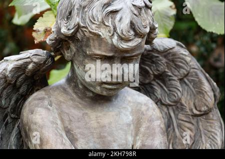 Ein kleiner Putto mit Engelsflügeln auf einem Grab sieht traurig auf dem Boden aus Stockfoto