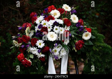 Bestattungskranz auf einem Friedhof mit bunten Blumen und Schleife auf einem Metallständer Stockfoto