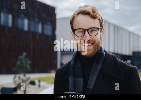 Ein junger rothaariger Typ, ein Geschäftsmann mit Brille, schaut in die Kamera vor dem Hintergrund eines urbanen Stils. Nahaufnahme des Porträts Stockfoto