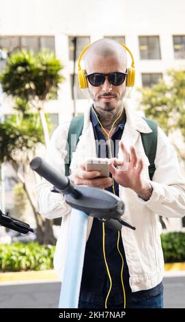 Vertikales Foto eines Mannes, der sein Handy benutzt, um einen Roller für öffentliche Verkehrsmittel zu entriegeln Stockfoto