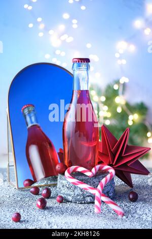Eine kleine Flasche Rosen, rosa Weinrebe auf einem Steinsockel, reflektiert in einem Lichtbogenspiegel. Weihnachtskonzert, Winterfest. Weihnachtsdekor im Winter, festlich Stockfoto