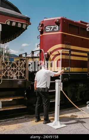 Eine alte rot-gelbe Diesellokomotive an der Kreuzung, an der der Zugführer die Reisenden am Bahnhof Conway Scenic leitet. North Conway Stockfoto