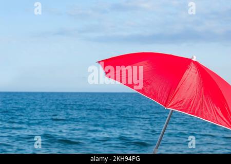 Roter Sonnenschirm am Strand der tropischen Insel. Farbenfroher Sonnenschirm am Strand am sonnigen Sommertag. Entspannung im Urlaub mit türkisfarbenem Meer und blauem Himmel Stockfoto