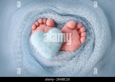 Beine, Zehen, Fuß und Fersen eines Neugeborenen. Blaues Strickherz in den Beinen Ihres Babys. Stockfoto