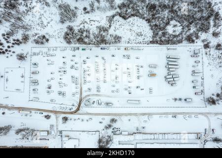 Blick aus der Vogelperspektive auf geparkte Autos auf dem Parkplatz nach Schneefall im Winter. Drohnenfoto. Stockfoto