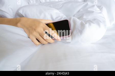 Frau schläft im Bett und Hand hält Handy. Frau, die im Schlafzimmer ein Smartphone benutzt. Sie schläft mit dem Smartphone. Ungleichgewicht zwischen Berufs- und Privatleben. Ungesunder Schlaf Stockfoto