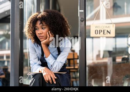 Junge afrikanische Frau hat traurige Stimmung mit wartendem Gast vor der Tür des Cafés, weil wegen einer Virusinfektion. Coronavirus und Quarantäne Stockfoto