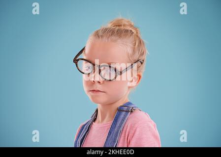 Wagen Sie es nicht, über meine neue Brille zu lachen...Studioaufnahme eines kleinen Mädchens mit Hipster-Brille auf blauem Hintergrund. Stockfoto