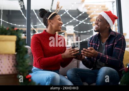 Geschenk, Paar und weihnachtsfeier auf dem Sofa von glücklichen, aufgeregten und liebevollen Menschen, die Freude, Jubel und Spenden in ihrem Zuhause teilen. Schwarzes Paar, Box und Stockfoto