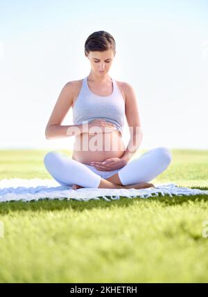 Halten Sie sich vor dem Baby in Topform. Eine schöne schwangere Frau, die im Freien Yoga macht. Stockfoto