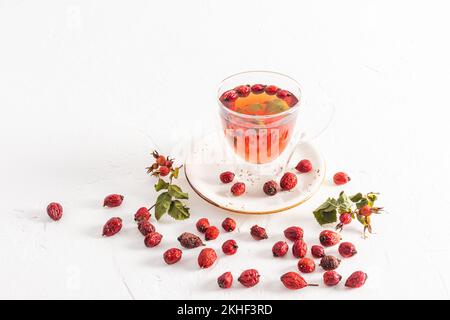 Glasbecher mit doppeltem Boden und heißem Vitamin-Tee von Rosenhüften auf weißem Hintergrund zwischen den Beeren. Nützlicher Tee gegen Erkältungen, erhöhte Immunität Stockfoto