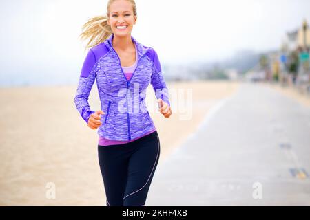 Ich fühle mich gut und sehe toll aus. Porträt einer jungen Frau, die in Strandnähe joggt. Stockfoto