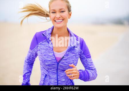 Sie lässt es einfach aussehen, fit zu werden. Porträt einer jungen Frau, die in Strandnähe joggt. Stockfoto