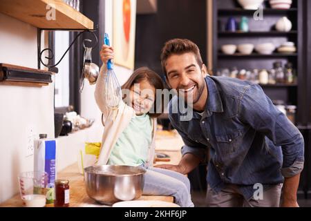 Ihr kleiner Helfer. Ein süßes kleines Mädchen, das ihrem Vater hilft, zu Hause Pfannkuchen zu backen. Stockfoto