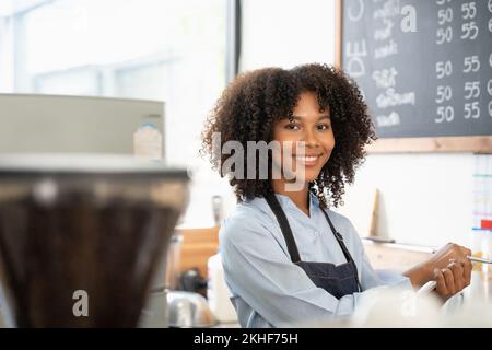 Porträt einer lächelnden jungen afroamerikanischen Kellnerin mit Schürze, die bereit ist, die Bestellung aufzunehmen Stockfoto