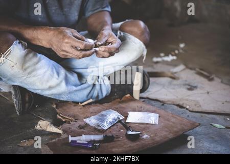 Die menschliche Hand eines Drogenabhängigen und eine Spritze mit Betäubungsmittelspritze liegen auf dem Boden, Welt-Anti-Drogen-Tag. Stockfoto