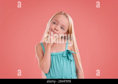 Lassen Sie mich darüber nachdenken... Studioaufnahme eines jungen Mädchens, das auf orangefarbenem Hintergrund posiert. Stockfoto