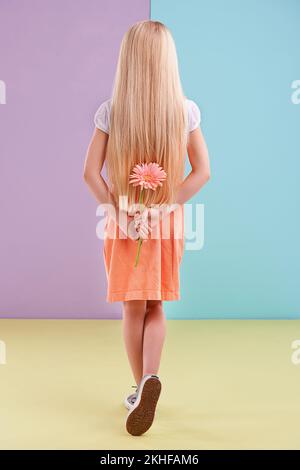 Sie hat eine Überraschung für mom... Ein kleines Mädchen mit einer Blume hinter ihrem Rücken. Stockfoto