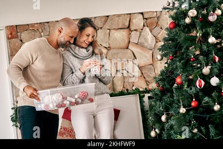Weihnachten, Liebe und ein Paar, das einen Baum schmückt, um die festliche Jahreszeit in ihrem gemeinsamen Zuhause zu feiern. Glücklich, lächeln und mit einem Mann dekorieren und Stockfoto