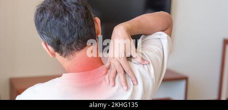 Ein Mann hat Nacken- und Schulterschmerzen, während er auf dem Sofa sitzt. Durch Fibromyalgie, Rheuma, kapuläre Schmerzen, Praxissyndrom und ergonomisches Konzept Stockfoto