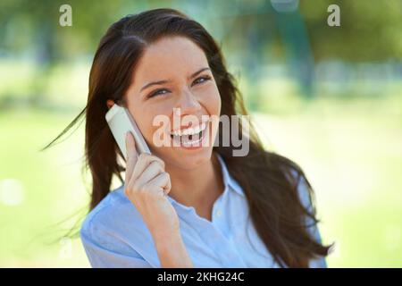 Lachen ist die beste Medizin. Porträt einer schönen jungen Frau, die lacht, während sie draußen telefoniert. Stockfoto