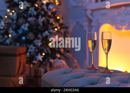 Nahaufnahme von zwei Champagnergläsern gefüllt mit Champagner vor einem Kamin und weihnachtsschmuck. Stockfoto