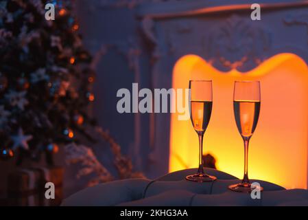 Nahaufnahme von zwei Champagnergläsern gefüllt mit Champagner vor einem Kamin und weihnachtsschmuck. Stockfoto