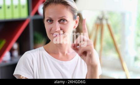 Eine lächelnde Frau, die in die Kamera schaut und mit dem Zeigefinger nach oben zeigt Stockfoto
