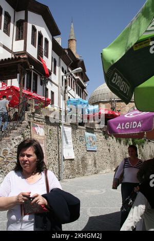 Straßenszene; Haupteinkaufsstraße; Beypazari; Türkei; eine Frau, die spaziert, Häuser auf einer Seite, Marktstände und ein Minarett. Stockfoto