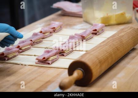 Der Schinken wird während der Konditorei auf ausgedrehtem Teig gelegt Stockfoto