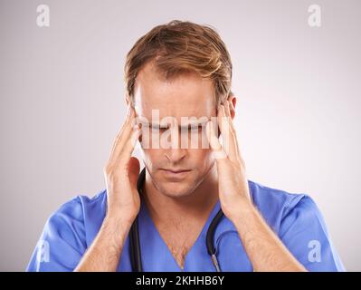 Kopfschmerzen im Gesundheitswesen. Studioaufnahme eines Arztes, der seinen Kopf vor Schmerzen hält. Stockfoto