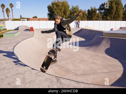 Sieh dir DAS an. Ein junger Mann, der auf seinem Skateboard im Skatepark Tricks macht. Stockfoto