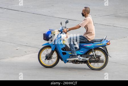 SAMUT PRAKAN, THAILAND, MÄRZ 02 2022, Ein Mann mit Gesichtsmaske fährt auf der Straße mit einem Motorrad Stockfoto