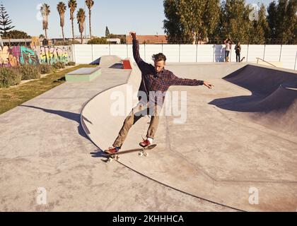 Das Leben am Rande. Ein junger Mann, der auf seinem Skateboard im Skatepark Tricks macht. Stockfoto