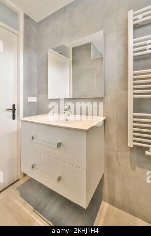 Regale mit Handtüchern und Trockengestell in der Nähe von Waschbecken mit Spiegeln und Badewanne in hellen Badezimmer der modernen Wohnung Stockfoto