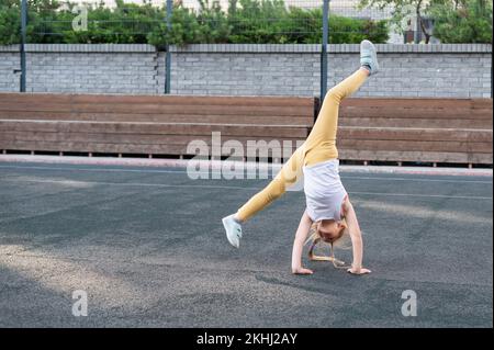 Kaukasisches Mädchen macht ein Karrenrad auf dem Sportplatz im Freien. Stockfoto