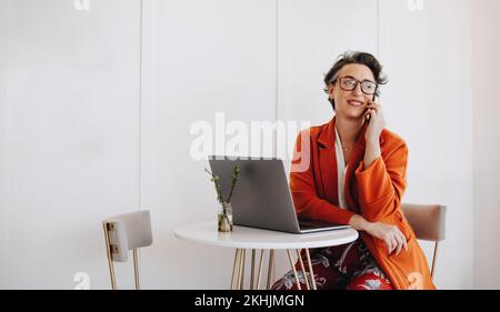 Reife Geschäftsfrau, die telefoniert, während sie an einem entfernten Standort arbeitet. Reife Geschäftsfrau, die mit einem ihrer Kunden Kontakt aufnimmt, während sie in einem Café arbeitet. Stockfoto