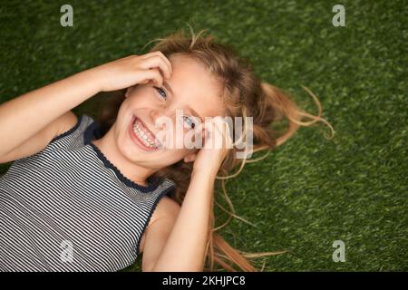 Outdoor-Spaß. Hochwinkel-Porträt eines süßen kleinen Mädchens, das auf dem Rücken auf dem Gras liegt. Stockfoto