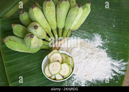 Bananenpulver auf Schüssel und rohe Banane - Bananenfrucht auf Blatthintergrund, alternatives Mehl, hausgemachtes grünes Bananenmehl für Kräutermedizin Naturkraut Stockfoto