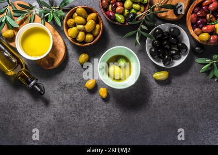 Verschiedene Oliven in der Schüssel auf dunklem Hintergrund. Oliven und eine Flasche Oliven. Draufsicht. Diät-Food-Konzept. Leckere Oliven. Stockfoto