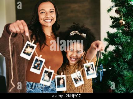 Weihnachten, Dekoration und Mutter und Mädchen mit Polaroid auf einem Baum für Liebe, Glück und Feiertagsfeier in einem Haus. Festlich, glücklich und Stockfoto