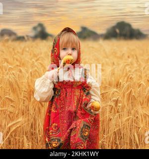 Kleines Mädchen im russischen nationalen Sarafan und ein Kokoschnik, der am Sommertag in einem goldenen Weizenfeld steht Stockfoto