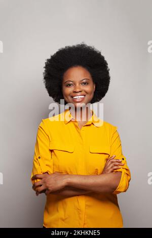 Freundliche, fröhliche, attraktive, junge afroamerikanische 25s-jährige Frau, die lächelt, Spaß hat, Spaß hat, die Hände auf weiß gekreuzt zu haben Stockfoto