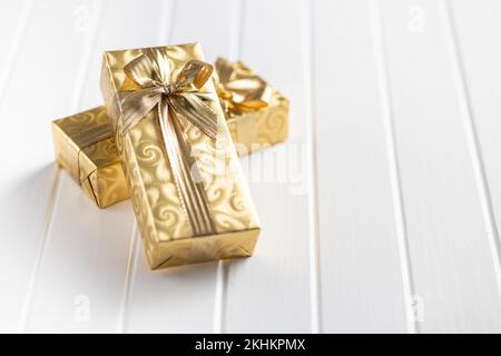 Geschenke in goldenes Papier eingewickelt mit einer goldenen Schleife auf dem weißen Tisch. Stockfoto