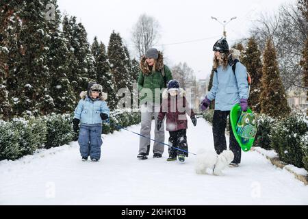 Winteraktivitäten im Freien für Familie und Freunde. Fröhliche Familie, Freunde, zwei Frauen, zwei Jungen und Hunde, Mütter und Söhne, die spazieren gehen und Spaß im Freien haben Stockfoto