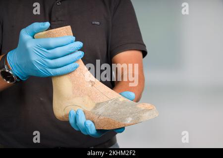 Nahaufnahme der Hände eines Schuhmachers, der eine einzelne Holzlast zur Herstellung von Intarsien oder Schuhen handhabt Stockfoto