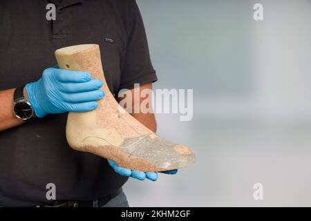 Nahaufnahme der Hände eines Schuhmachers, der eine einzelne Holzlast zur Herstellung von Intarsien oder Schuhen handhabt Stockfoto